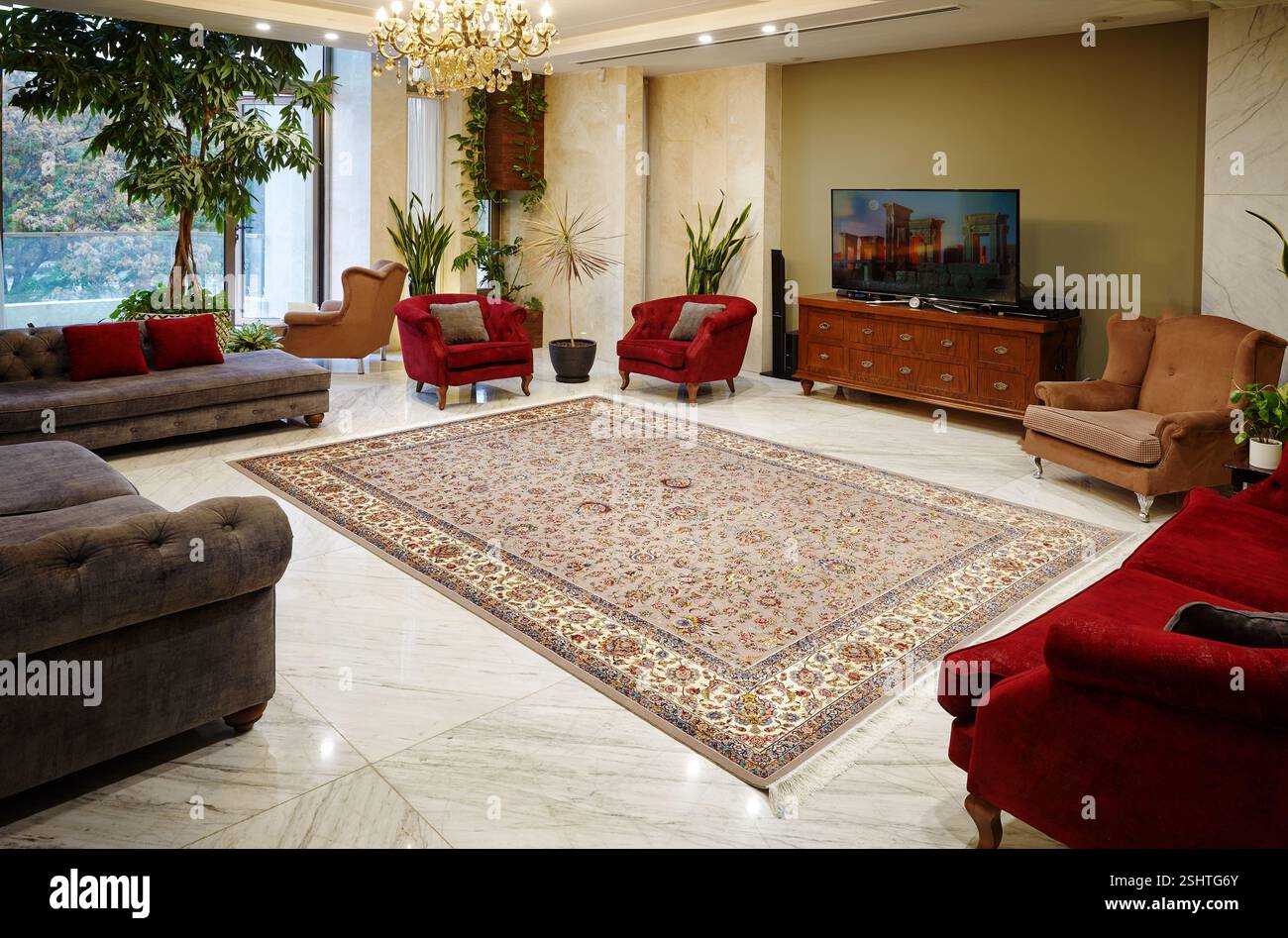 Elegante interno del soggiorno con un tradizionale tappeto persiano, divani classici, pavimento in marmo e piante interne. Foto Stock