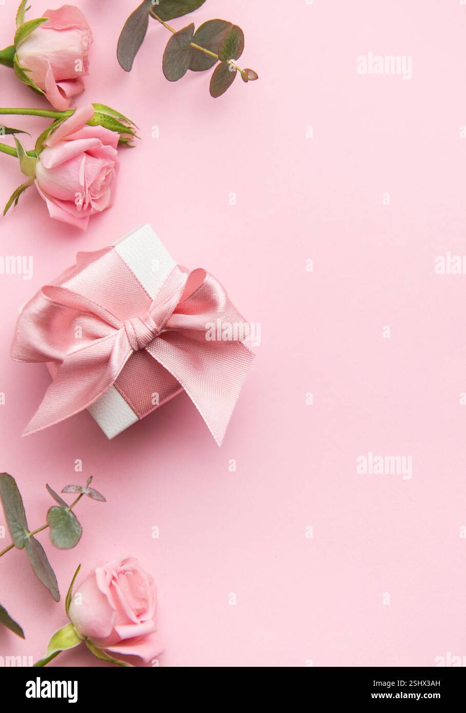 Elegante confezione regalo con nastro rosa e rose su sfondo rosa, per creare un'atmosfera romantica per san valentino o per la festa della mamma Foto Stock