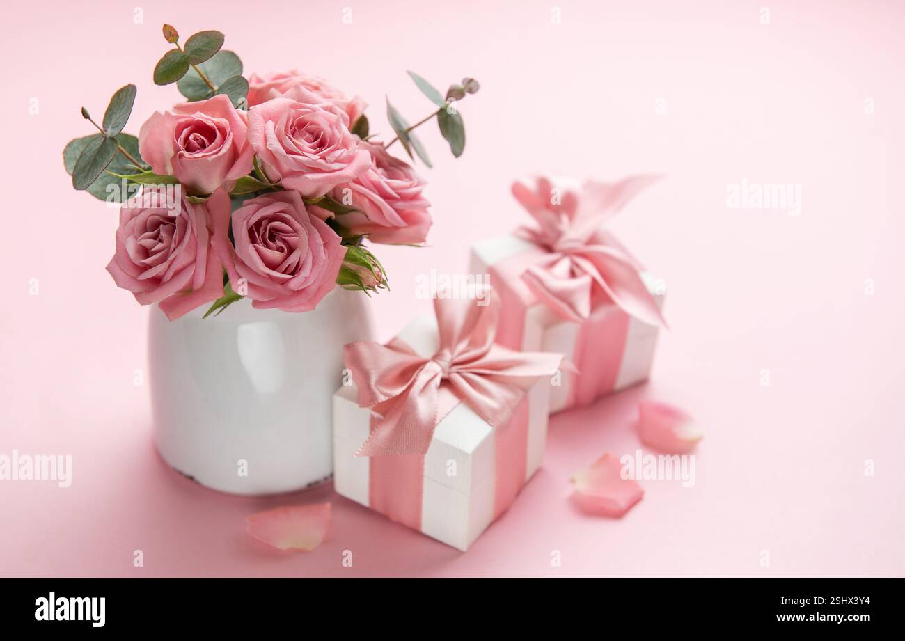 Bouquet di rose rosa in vaso bianco che decora scatole regalo con nastri rosa per san valentino, festa della mamma o compleanno su sfondo rosa Foto Stock