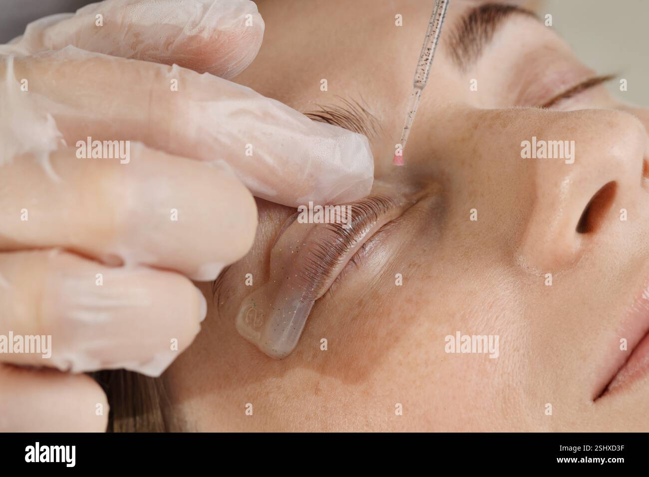Procedura di laminazione delle ciglia. Estetista che attacca le ciglia della donna per immergerle nel salone di bellezza, primo piano Foto Stock