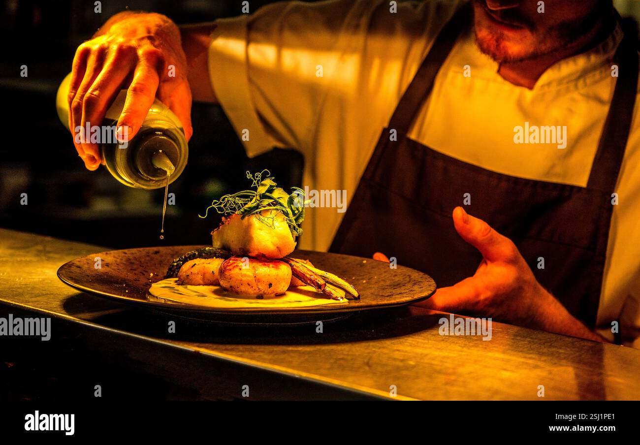 Uno chef spruzza olio d'oliva su un pasto preparato al momento in un ristorante del Regno Unito Foto Stock