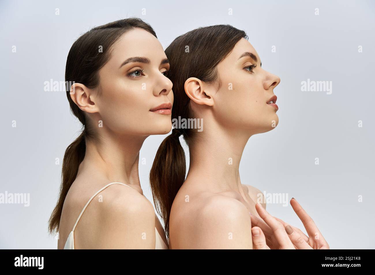 Due bellissime sorelle gemelle si mettono in posa uno dietro l'altro, mettendo in risalto le loro caratteristiche eleganti e il loro legame. Foto Stock