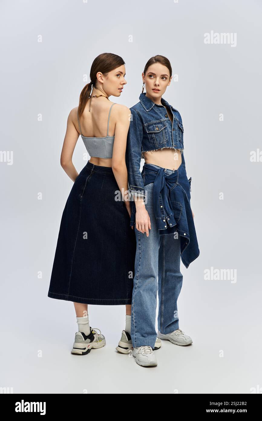 Due bellissime sorelle si mettono in posa uno contro l'altro, mettendo in risalto i loro esclusivi outfit in denim in uno studio. Foto Stock