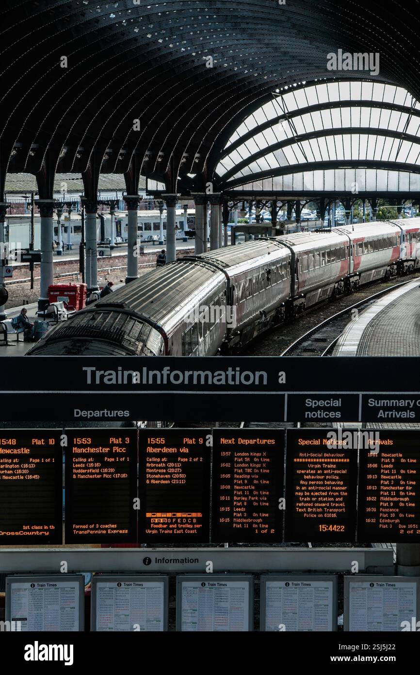 Iconica stazione ferroviaria con architettura curva, scheda di partenza digitale e un treno fisso sotto un grande tetto ad arco a York, Regno Unito. Foto Stock