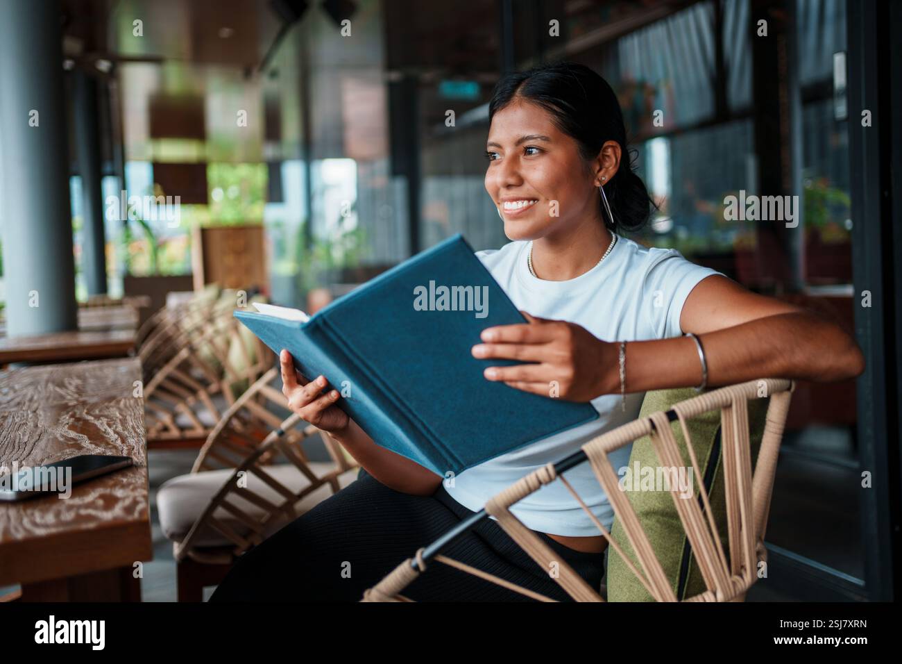 Una donna sorridente ama leggere un libro mentre si rilassa in un caffè accogliente e confortevole Foto Stock