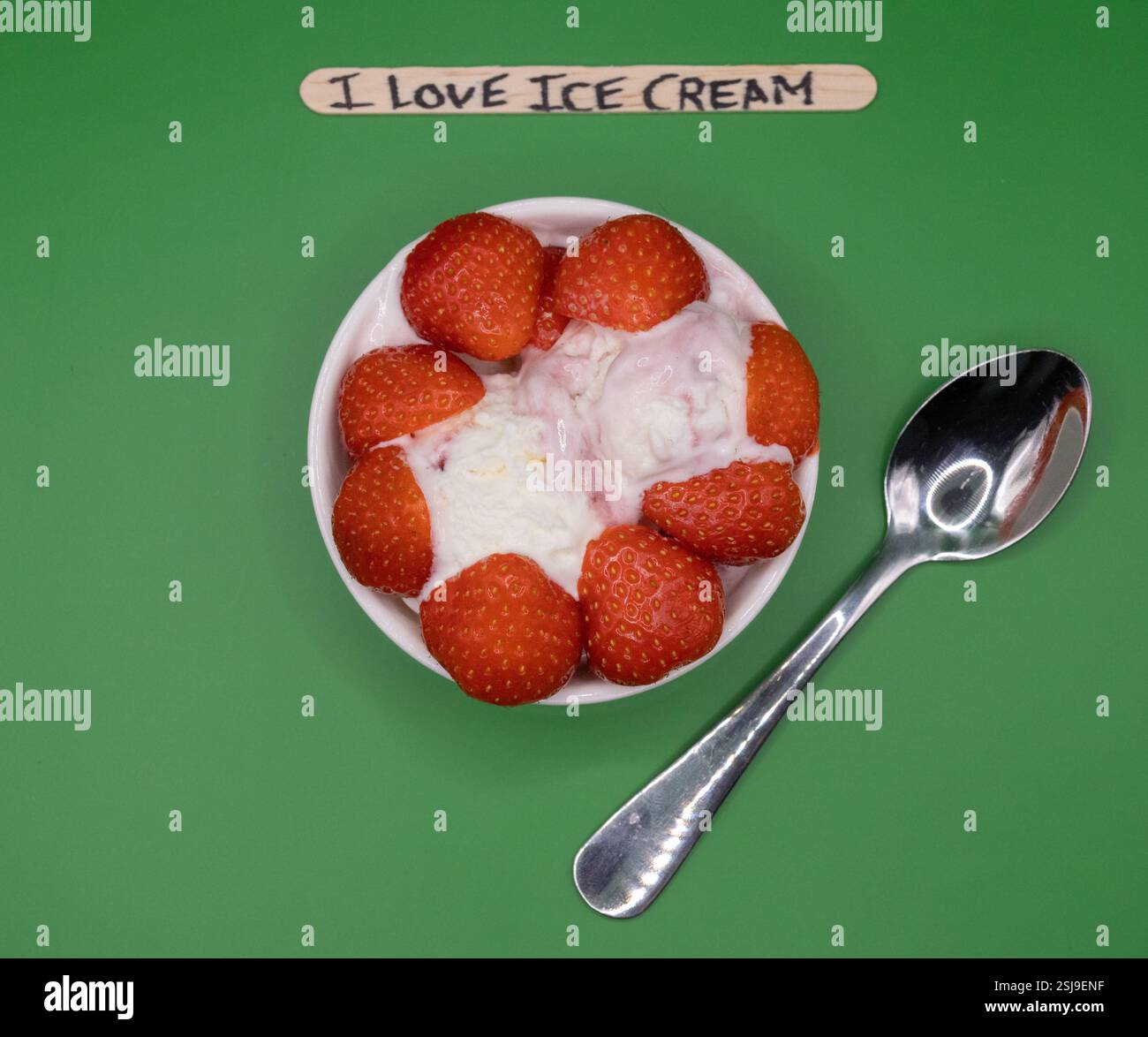 Una ciotola di gelati e fragole, con bastoncini di papavero scritti a mano su sfondo verde. Foto Stock