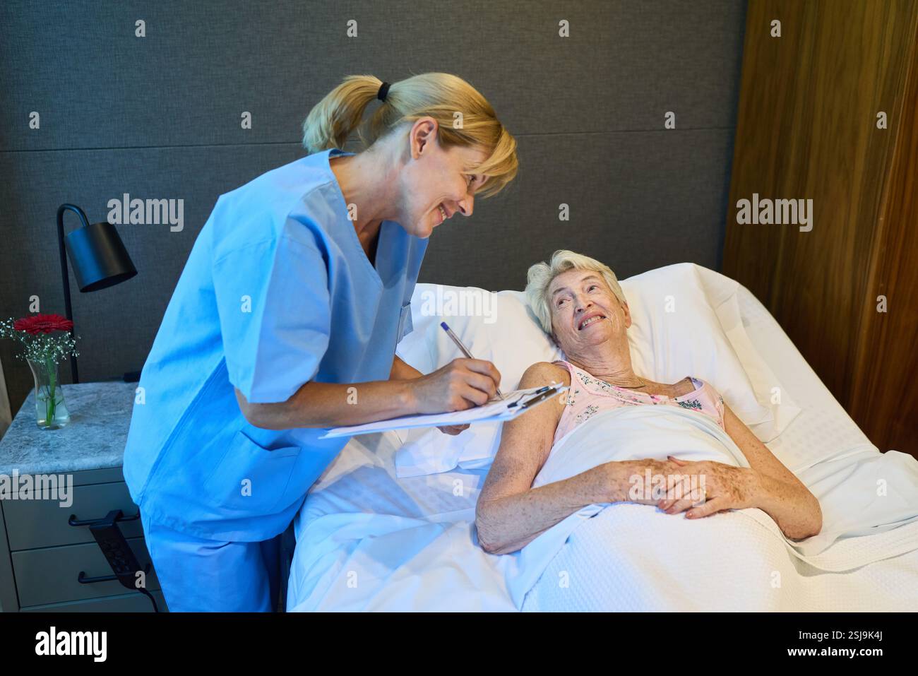 Un infermiere comunica con un paziente anziano, promuovendo un'atmosfera compassionevole all'interno di una struttura di riabilitazione. L'ambientazione mette in risalto le profess Foto Stock