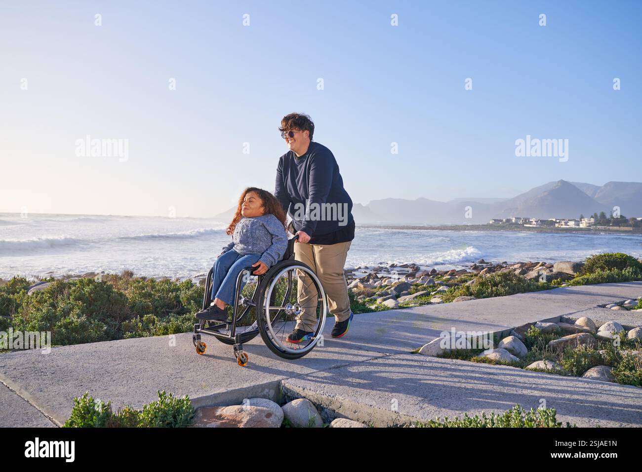 Donna che spinge un amico in sedia a rotelle sul sentiero Foto Stock