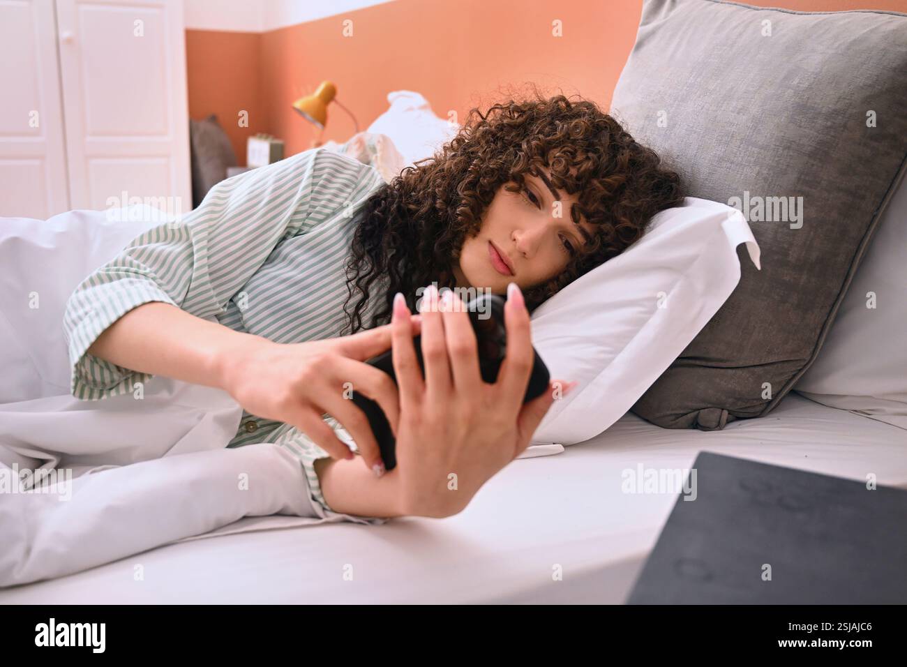 Donna con smartphone a letto Foto Stock