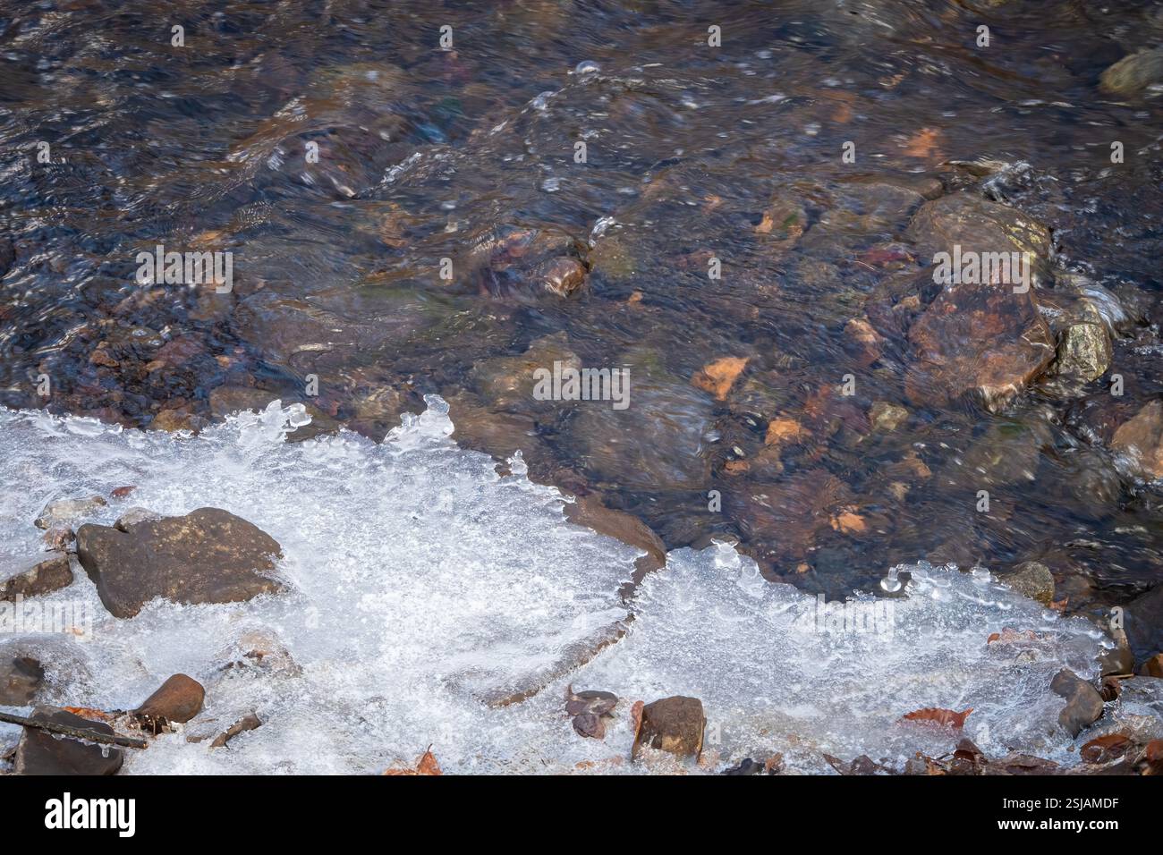 L'acqua fluente incontra il ghiaccio sul bordo di un torrente Foto Stock