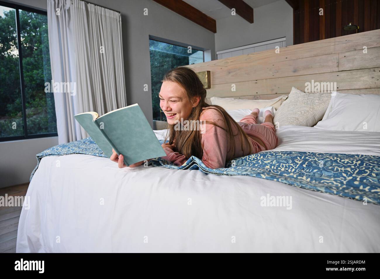 Ragazza sorridente (12-13) che legge a letto Foto Stock