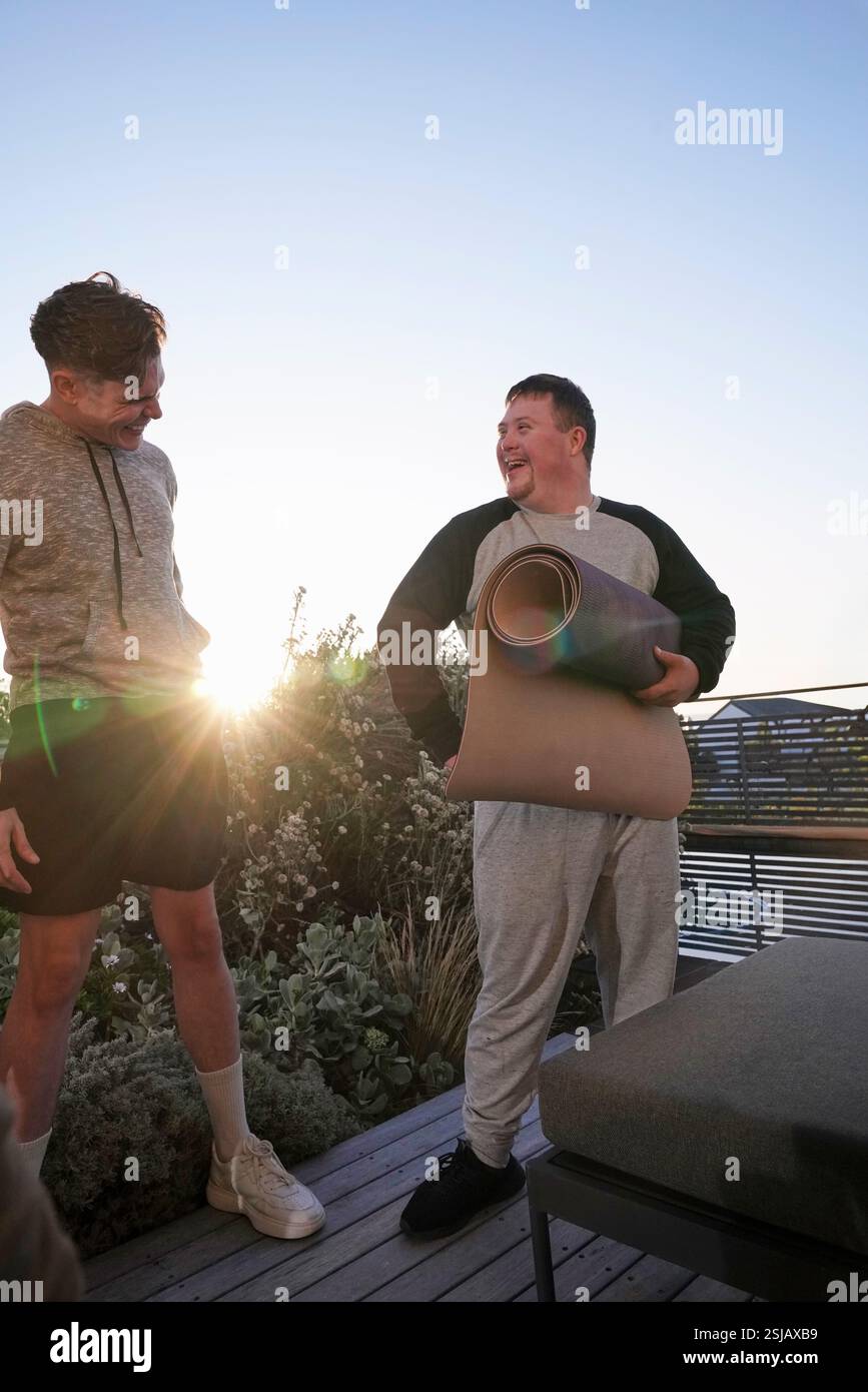 Uomini sorridenti con tappetini da yoga sul patio Foto Stock