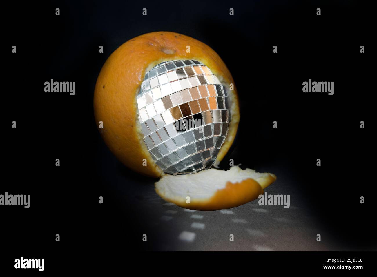 Immagine surreale creativa di un'arancia parzialmente sbucciata per rivelare una sfera da discoteca all'interno. La superficie riflettente della sfera da discoteca proietta sequenze di luce. Foto Stock