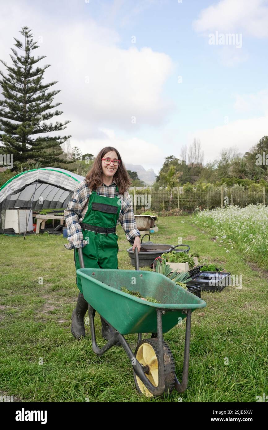 Agricoltrice che spinge carriola in giardino Foto Stock
