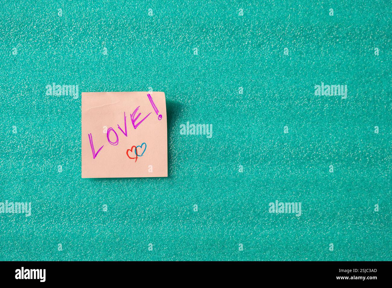 Una nota adesiva rosa con "Love" scritta in grassetto, su sfondo verde. Un concetto vibrante che simboleggia affetto e positività. Foto Stock
