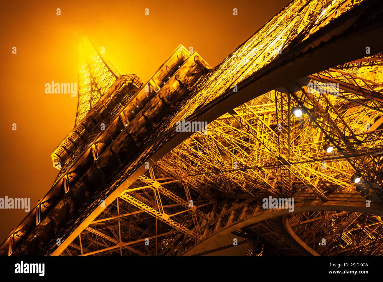 Vista ad angolo basso dal livello del suolo che guarda sulla Torre Eiffel illuminata, in una fredda e nebbiosa serata invernale. Parigi Foto Stock