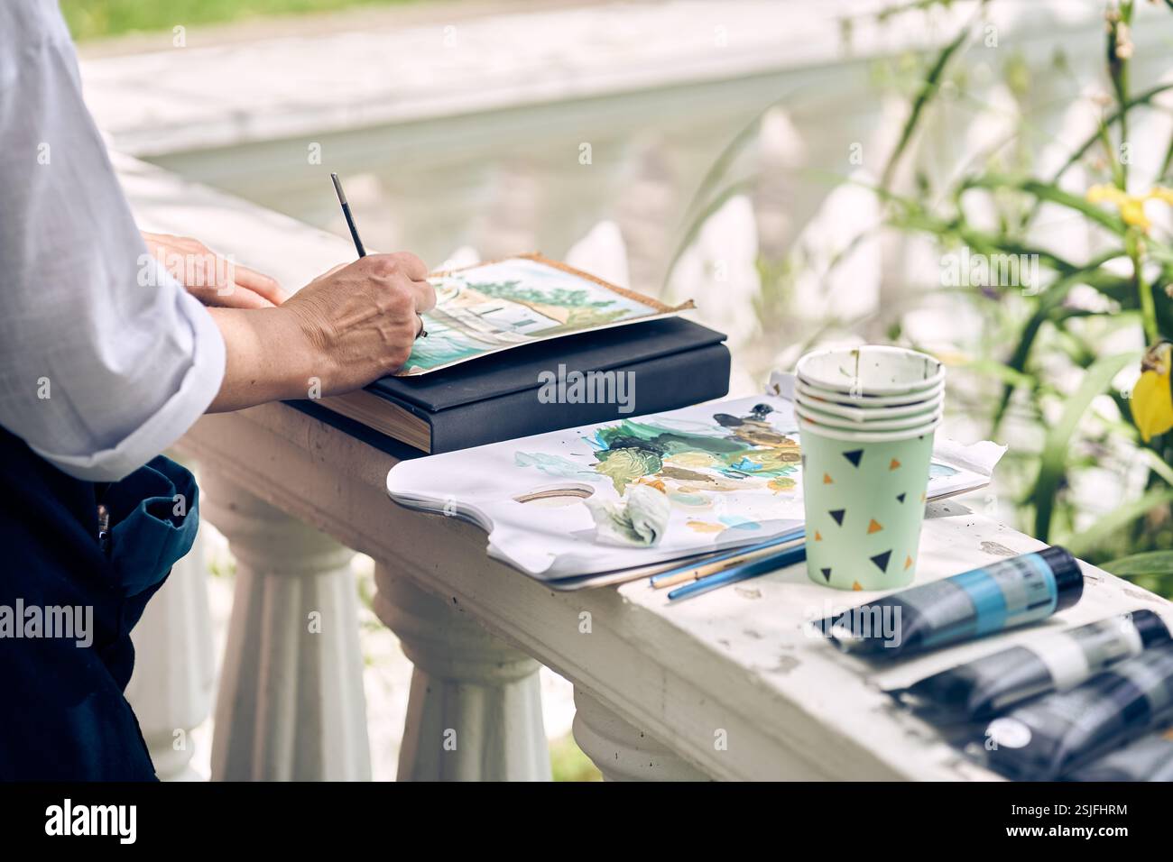 Un primo piano di un artista che dipinge all'aperto. Le forniture artistiche sono posizionate accanto al disegno. Foto di alta qualità Foto Stock