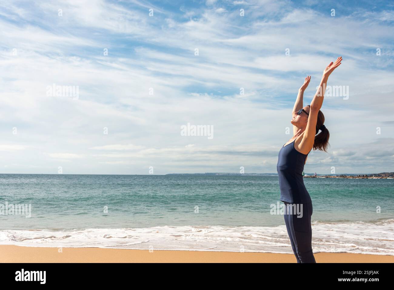 donna sportiva in riva al mare con le braccia alzate Foto Stock