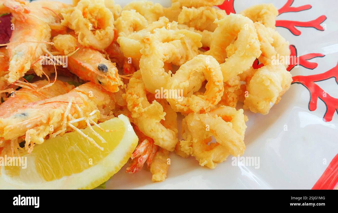 Deliziosi calamari e gamberi fritti serviti su un piatto bianco con una fetta di limone, per un'allettante delizia di pesce Foto Stock