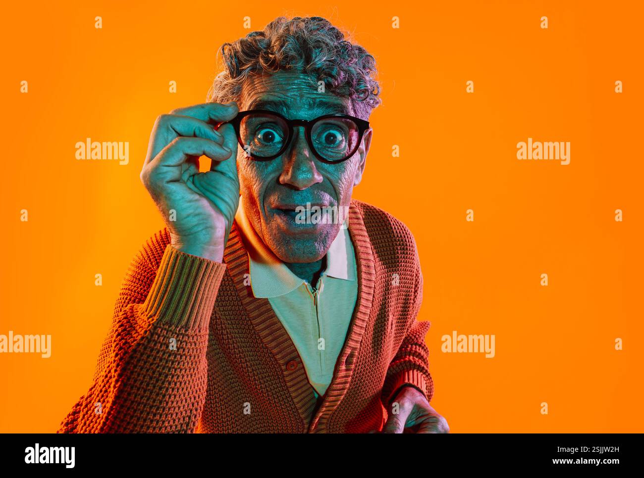 Uomo anziano che posa in studio. Un uomo anziano divertente con un pullover medio che poggia su sfondi colorati. Foto in studio con luci colorate in gel. Foto Stock