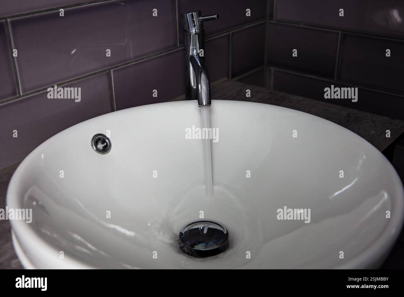 Lavabo circolare da banco bianco in ceramica con rubinetto cromato e acqua in uscita Foto Stock