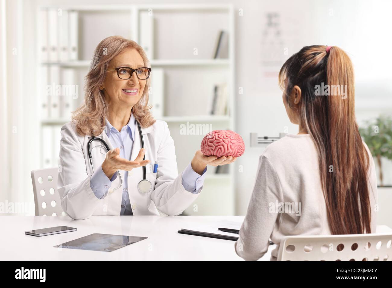 Medico neurologo donna che tiene un modello cerebrale e parla con una donna in ufficio Foto Stock
