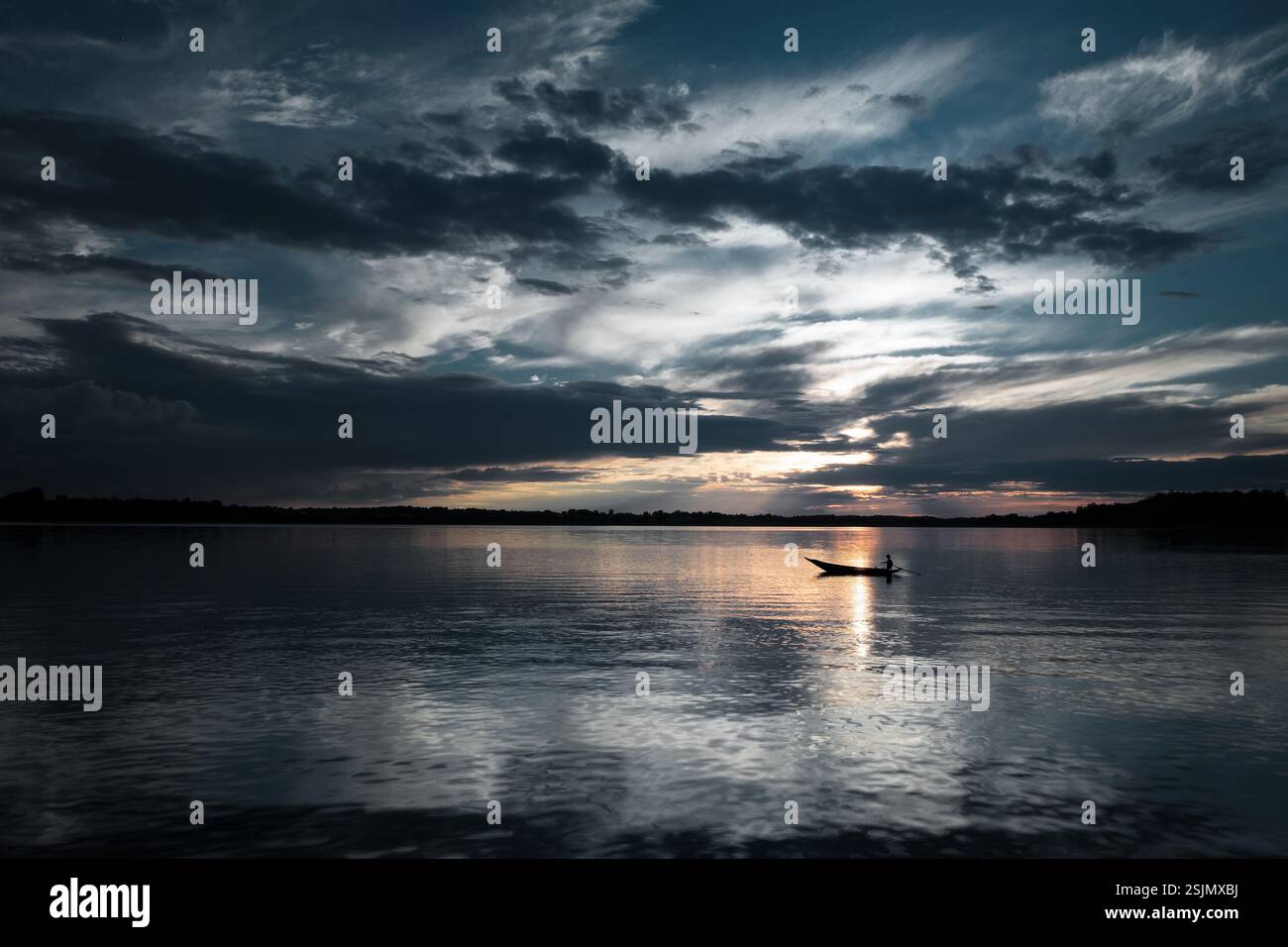 Una barca solitaria galleggia su un lago tranquillo, sagomato contro un cielo lunare con riflessi dorati del tramonto sull'acqua Foto Stock