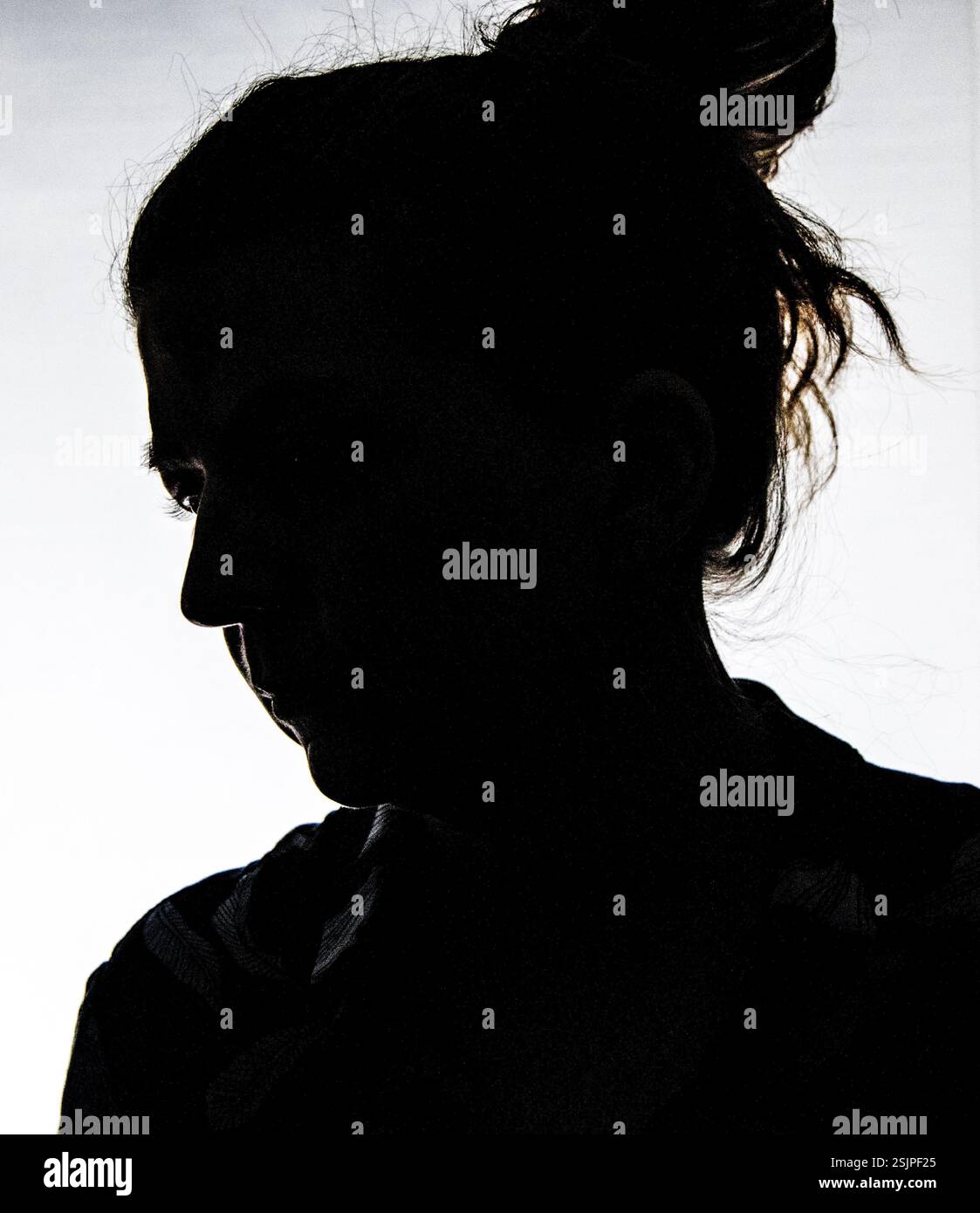 Silhouette di una donna su uno sfondo luminoso. Il contorno scuro oscura i tratti del viso, creando un effetto misterioso e drammatico. Foto Stock