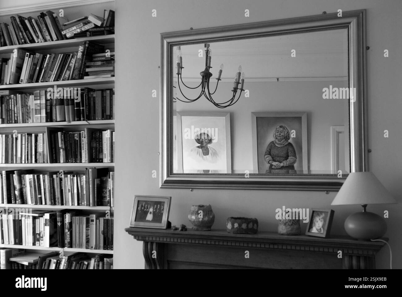 Interni, casa familiare di classe media. Mantello e ornamenti, scaffale a libro completo non ordinato. Ritratti sulla parete riflessi in un grande specchio dorato incorniciato sopra il camino Cardiff Galles anni '2014 2010 UK HOMER SYKES Foto Stock