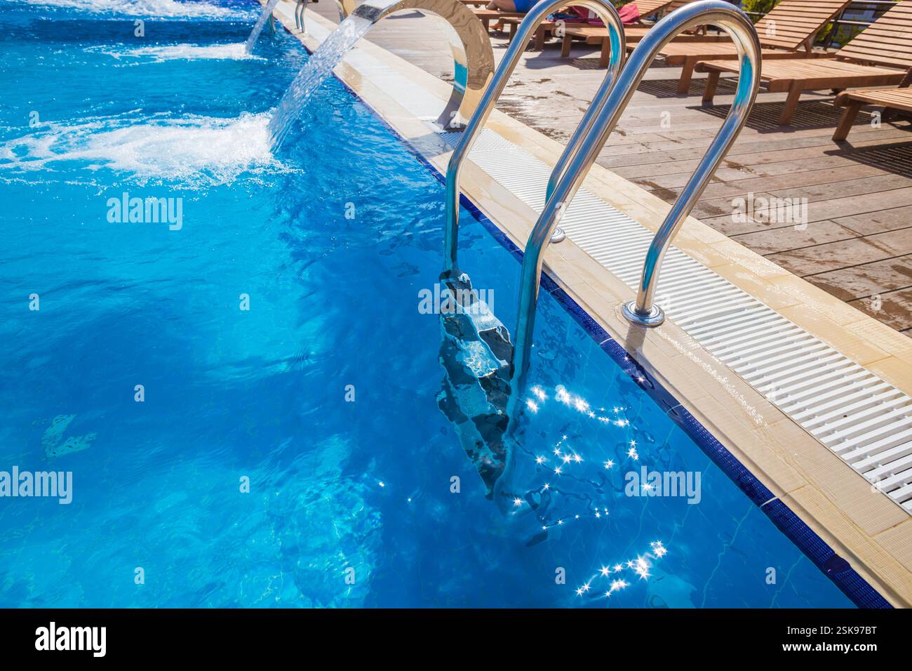 Rilassante vista sulla piscina con piscina azzurra e scala con lettini in un ambiente soleggiato all'aperto Foto Stock