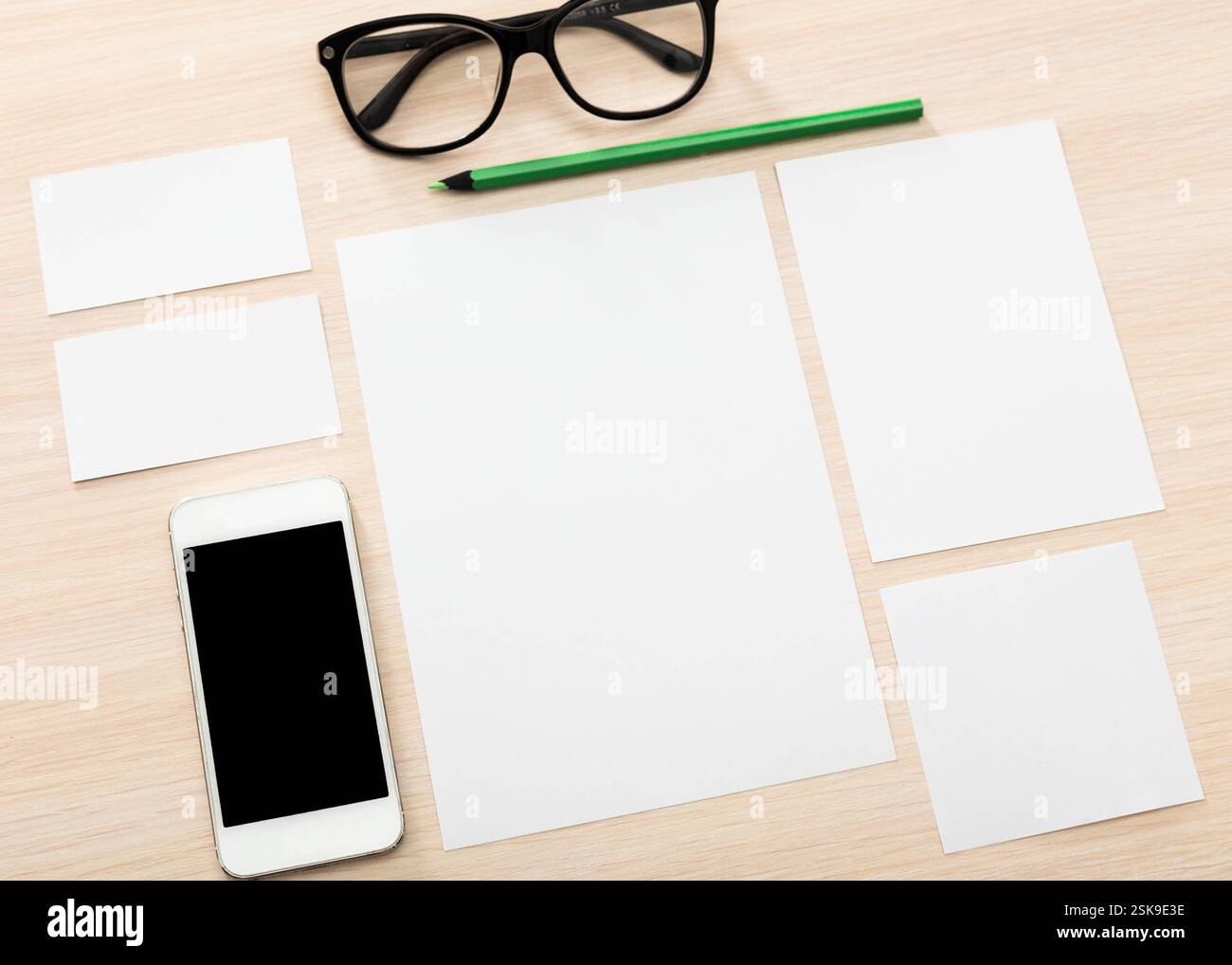 Disposizione dello spazio di lavoro su una scrivania in legno con carta vuota, occhiali e smartphone in un ambiente ben illuminato Foto Stock