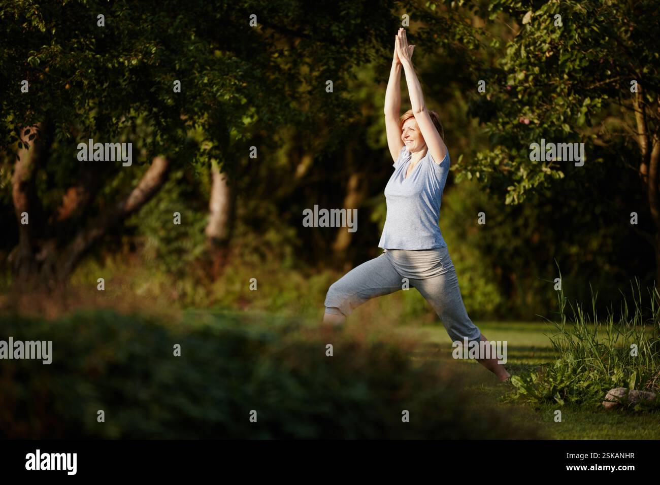 Felice, donna e stretching per yoga su erba di consapevolezza, guarigione spirituale e pace. Sorridi, persona e riscalda i muscoli con una posa da guerriero Foto Stock
