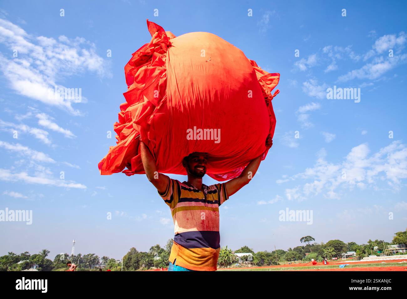 Un lavoratore porta un panno colorato sulla testa mentre si dirige verso la fabbrica dopo che si è asciugato. Narsingdi, Bangladesh. Foto Stock
