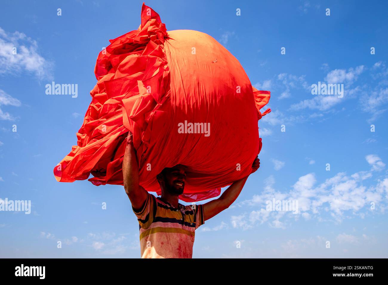 Un lavoratore porta un panno colorato sulla testa mentre si dirige verso la fabbrica dopo che si è asciugato. Narsingdi, Bangladesh. Foto Stock