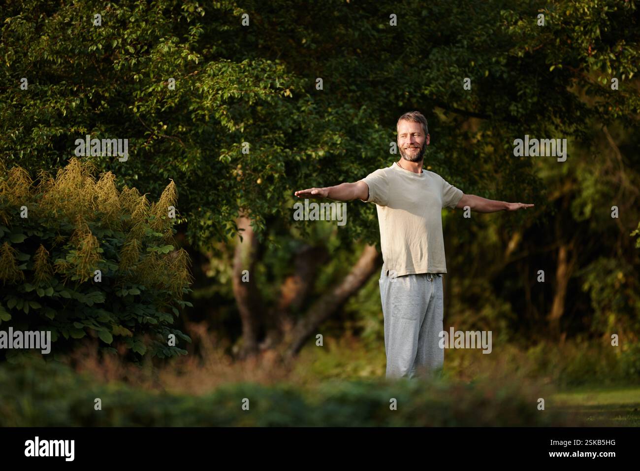 Sorridi, uomo e stretching per yoga sull'erba con consapevolezza, guarigione spirituale e pace in giardino. Pensare, persona maschile e riscaldare muscoli con Foto Stock