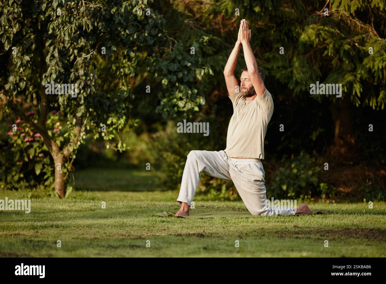 Uomo, stretching e yoga sull'erba all'aperto con consapevolezza, guarigione spirituale e pace. Persona, occhi chiusi e riscaldare muscoli con posa guerriera per Foto Stock