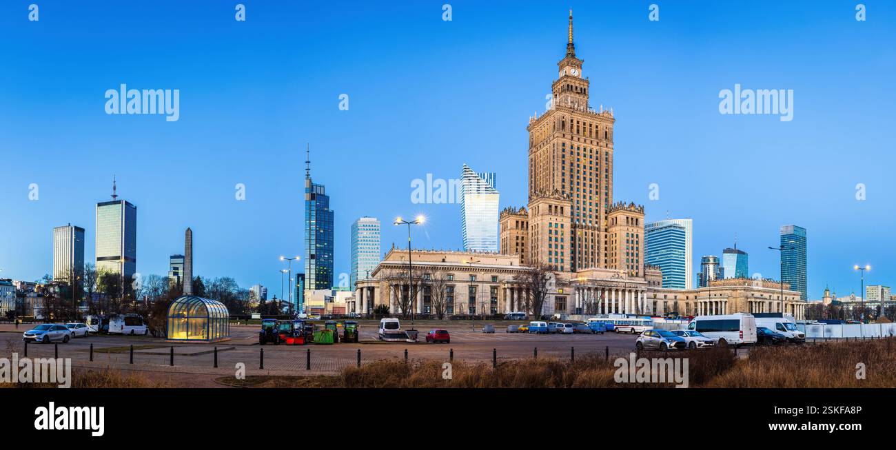 Il centro di Varsavia prima dell'alba fonde i moderni grattacieli con l'iconico Palazzo della Cultura. I lampioni si illuminano, riflettendo sulle torri di vetro Foto Stock