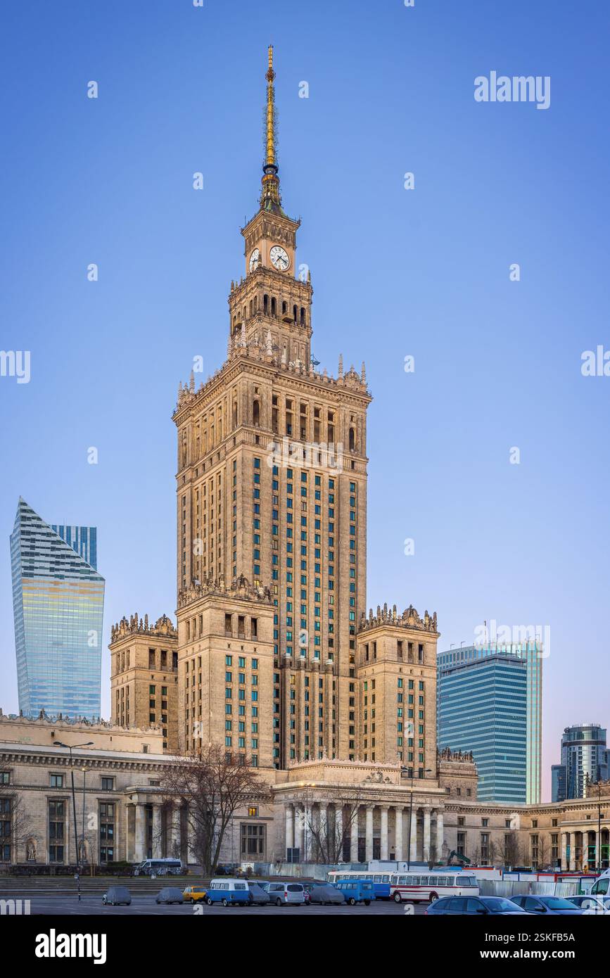 Il centro di Varsavia prima dell'alba fonde i moderni grattacieli con l'iconico Palazzo della Cultura. I lampioni si illuminano, riflettendo sulle torri di vetro Foto Stock
