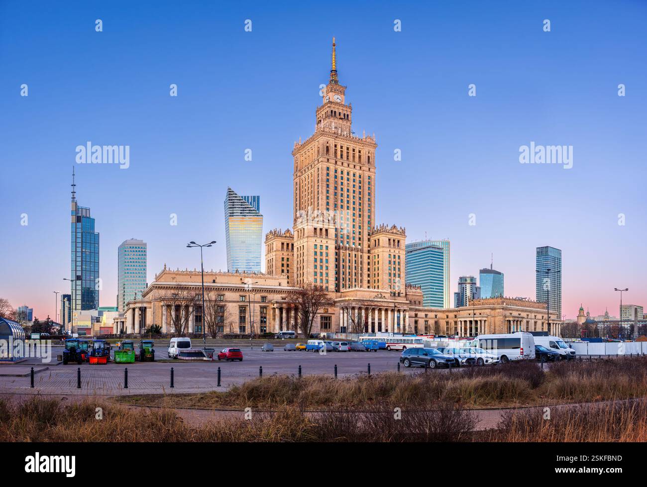 Il centro di Varsavia prima dell'alba fonde i moderni grattacieli con l'iconico Palazzo della Cultura. I lampioni si illuminano, riflettendo sulle torri di vetro Foto Stock