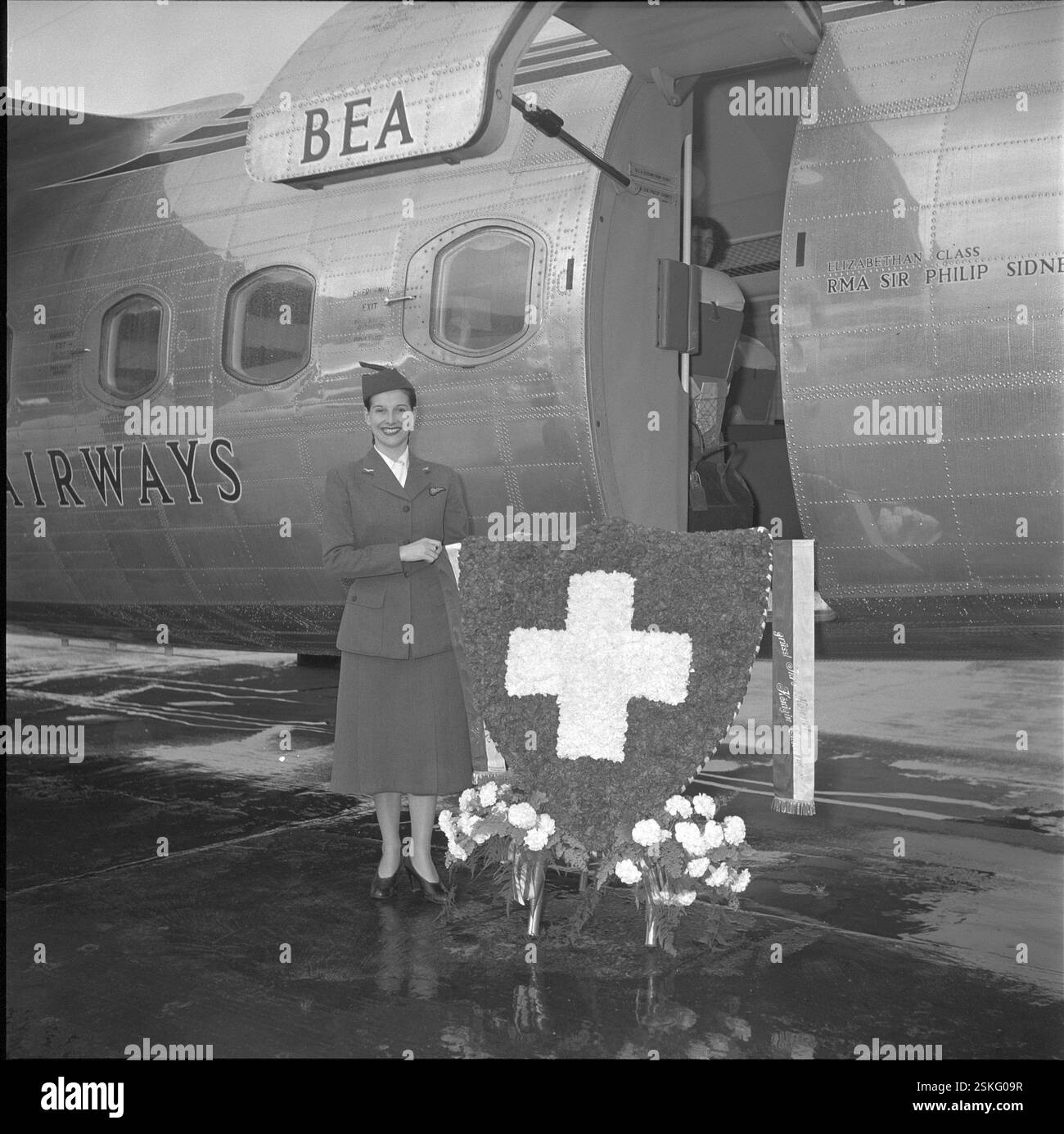 Schweizer Blumen für die englische Königin: Werbung zur Filmpremiere von 'Because You're mine' mit Mario Lanza a Londra#fiori svizzeri per la Regina britannica: Promozione per l'apertura del film 'Because You're mine' con Mario Lanza a Londra--- BEA-Stewardess mit Blumengruss, Schweizer Kreuz, Flughafen Zürich-Kloten 1952#BEA assistente di volo con fiori, swiss cross, Zurigo DUKAS-Kloten, 1952-Kloten Airport Foto Stock