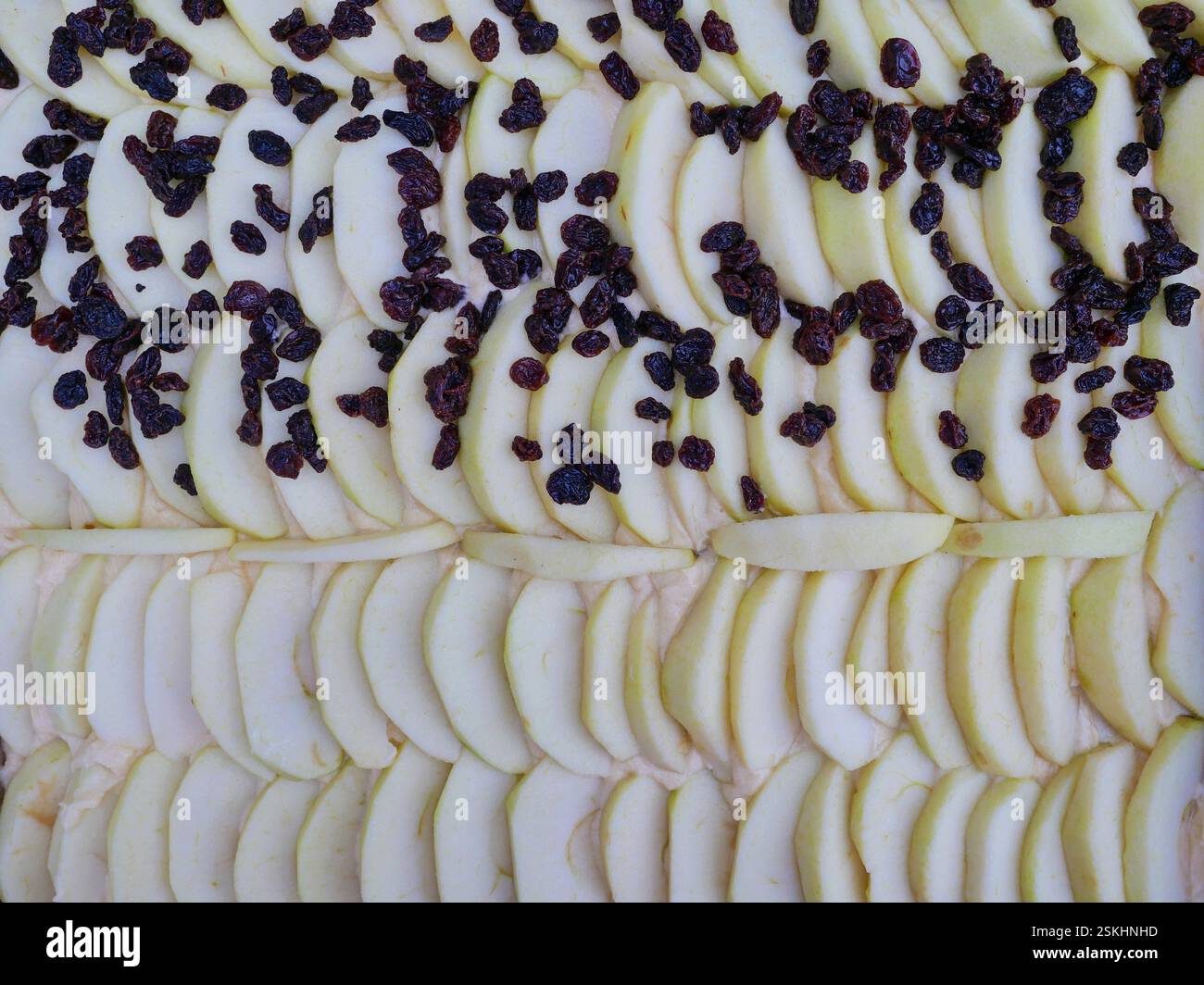 Torta di mele prima della cottura: Fette di mele ben posizionate sull'impasto, cosparse di uvetta. Una ricetta tradizionale per una delizia fruttata fatta in casa. Foto Stock