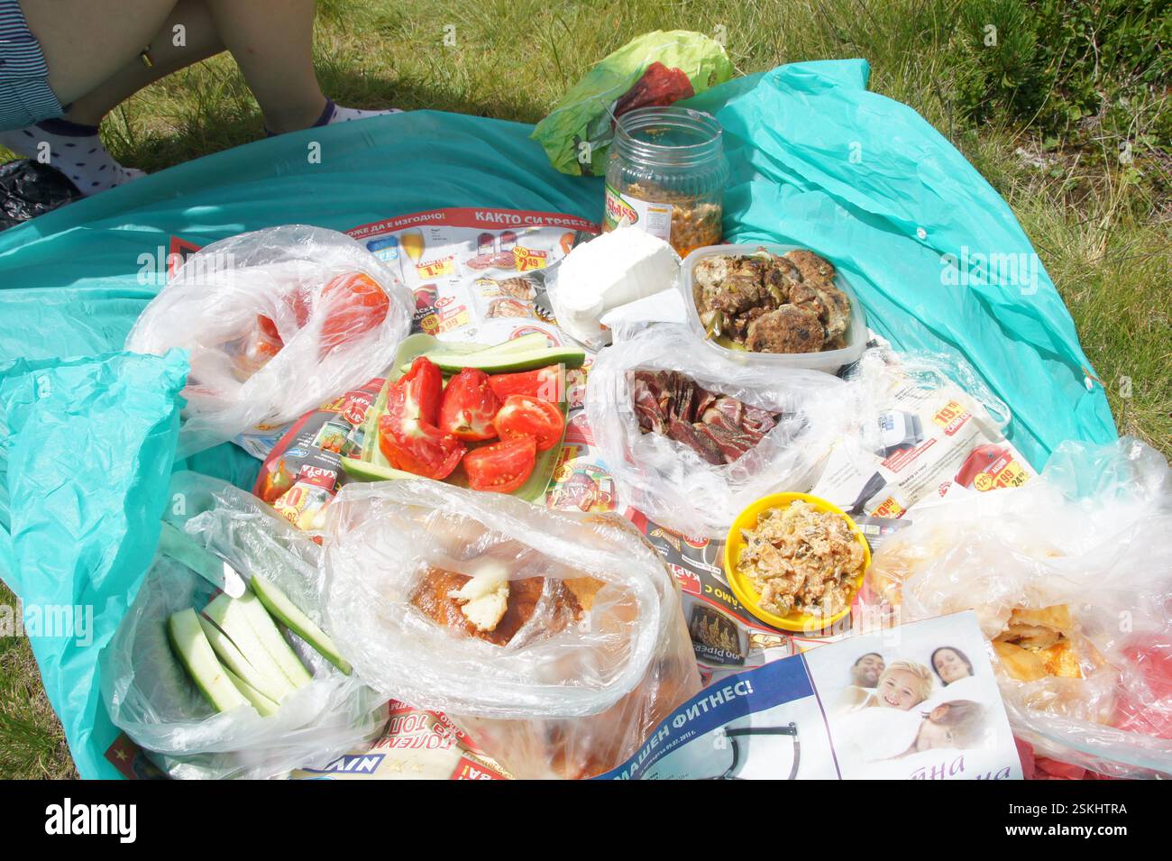 BULGARIA picnic si stende su una tela cerata blu con vari cibi e bevande. I sacchetti di plastica contengono pomodori, cetrioli e pane. Una ciotola gialla contiene uno spuntino. Foto Stock
