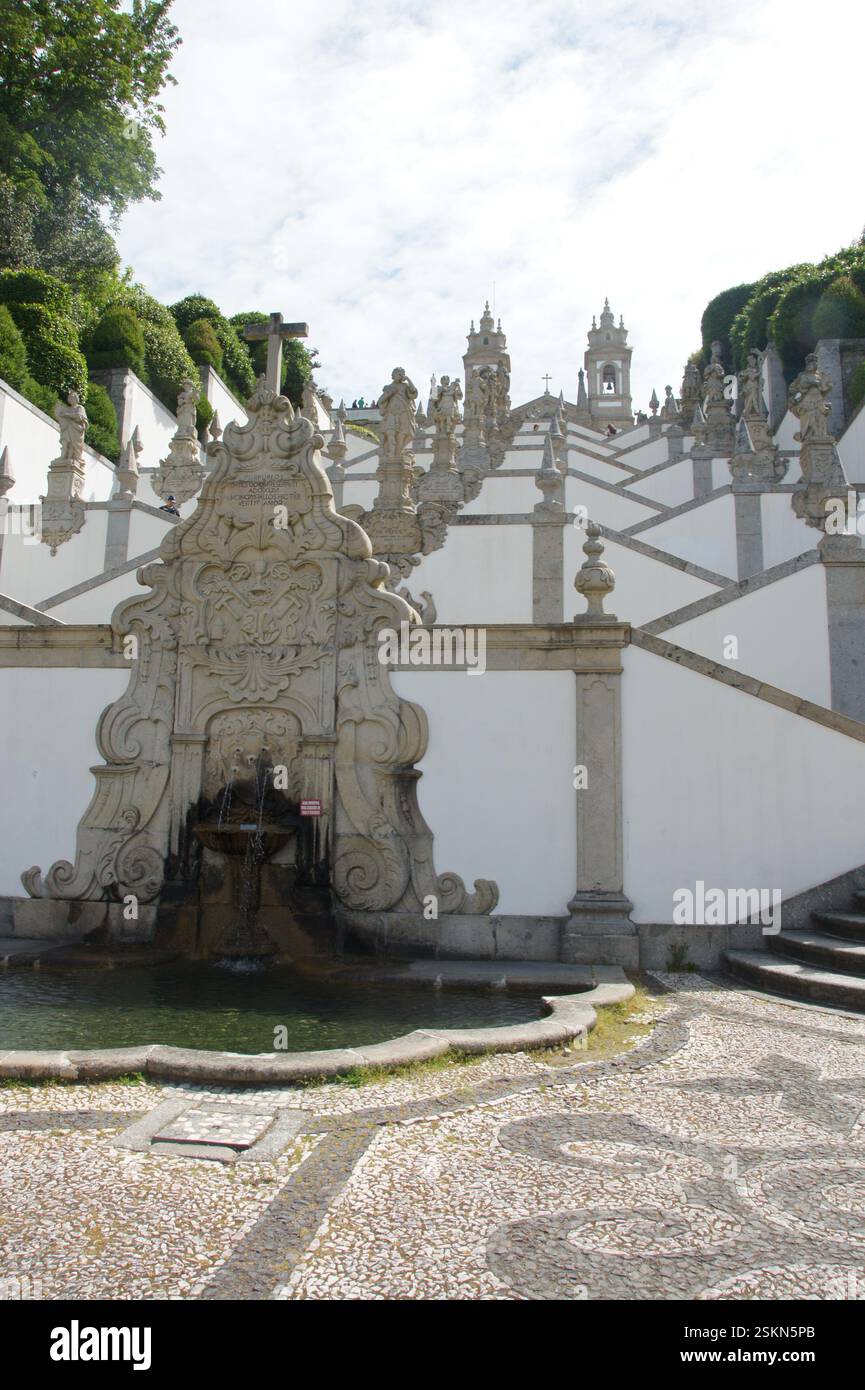La scalinata in pietra sale drammaticamente fino a una chiesa barocca incontaminata a Braga, Portogallo. Un simbolo di fede e pellegrinaggio. Una pittoresca fontana abbellisce i bassifondi Foto Stock