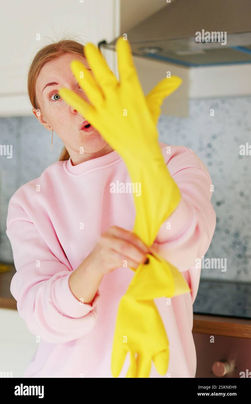 la ragazza indossa guanti di gomma gialli prima di pulire la casa Foto Stock