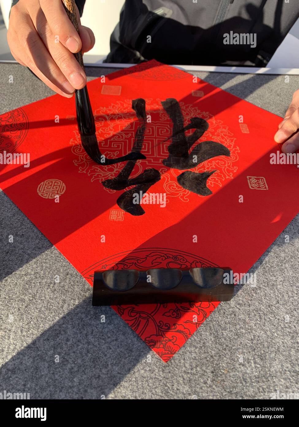 Uomo che dipinge calligrafia cinese su carta rossa Foto Stock