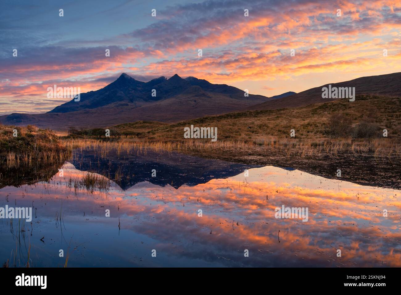 Splendida isola di Skye al tramonto con le montagne Cuillin che si riflettono in un tranquillo Loch Nan Eilean. Foto Stock