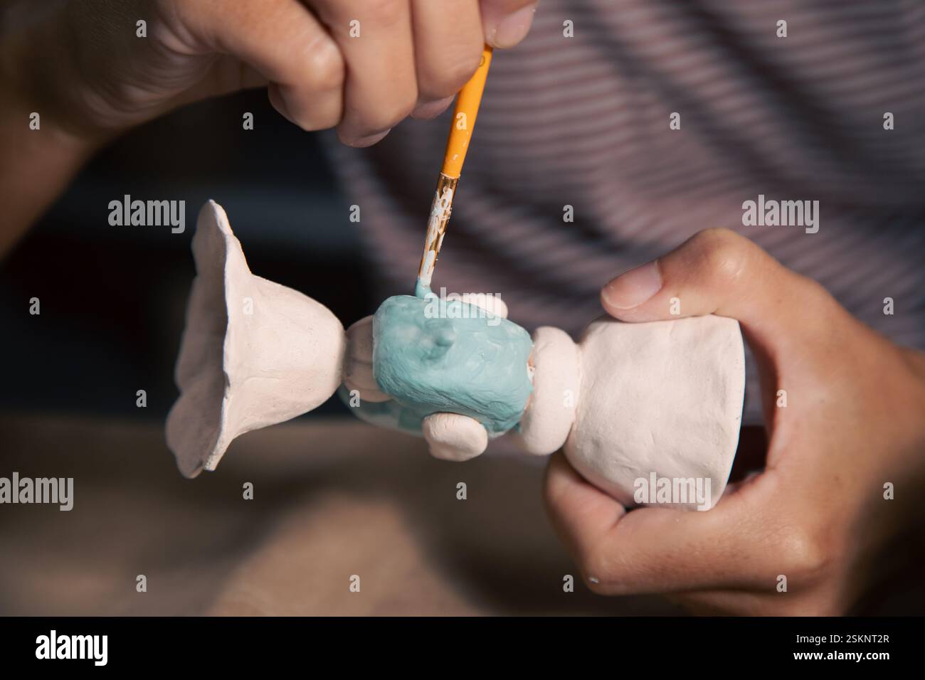Primo piano di una donna seduta a un tavolo in uno studio di ceramica che glassa un candelabro di argilla Foto Stock
