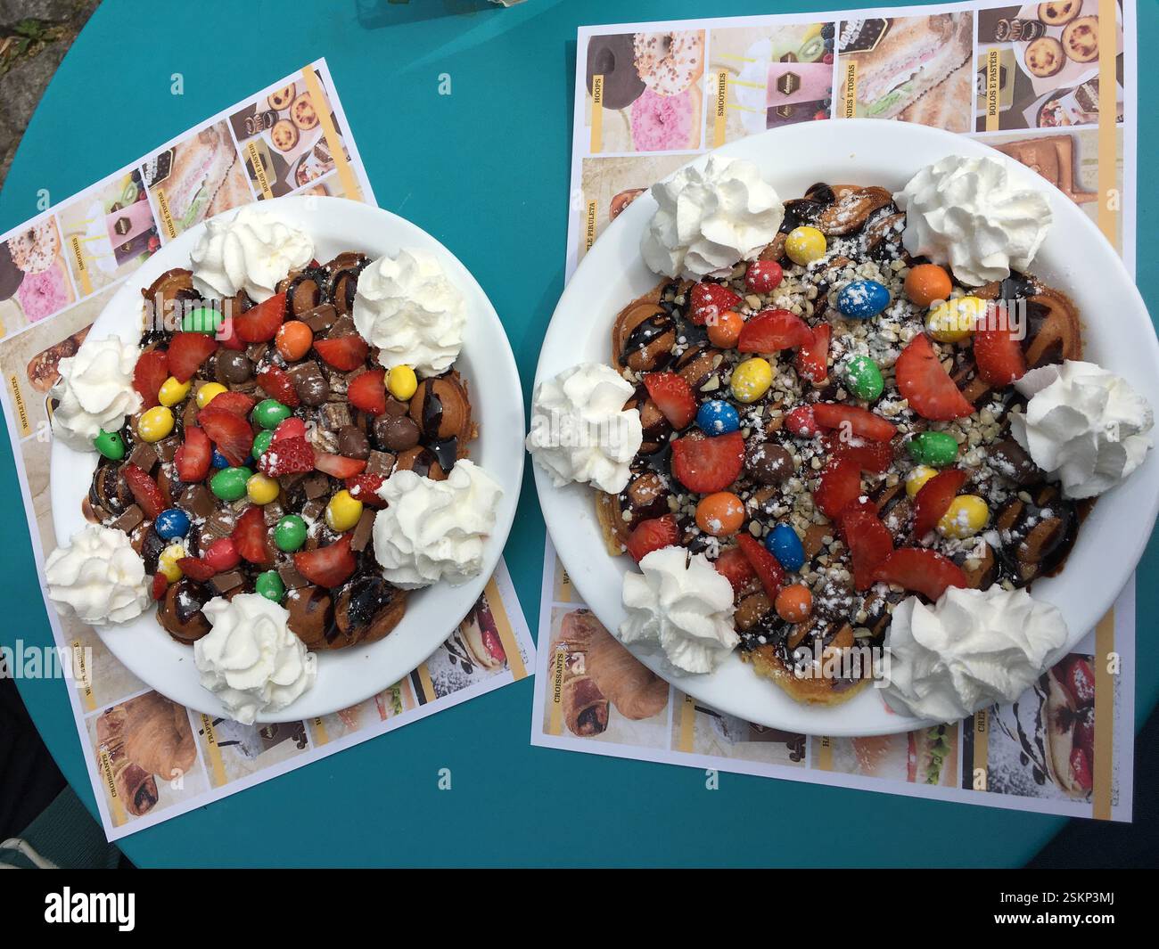 Due piatti di waffle con panna montata, fragole, salsa al cioccolato e caramelle colorate. Braga, Portogallo. Dolce e appagante. A. Foto Stock