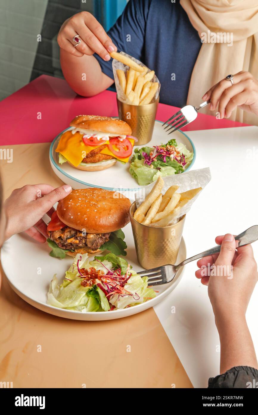 Fotografia di hamburger gourmet in un ambiente da caffetteria, amici che si godono un pasto insieme. Foto Stock