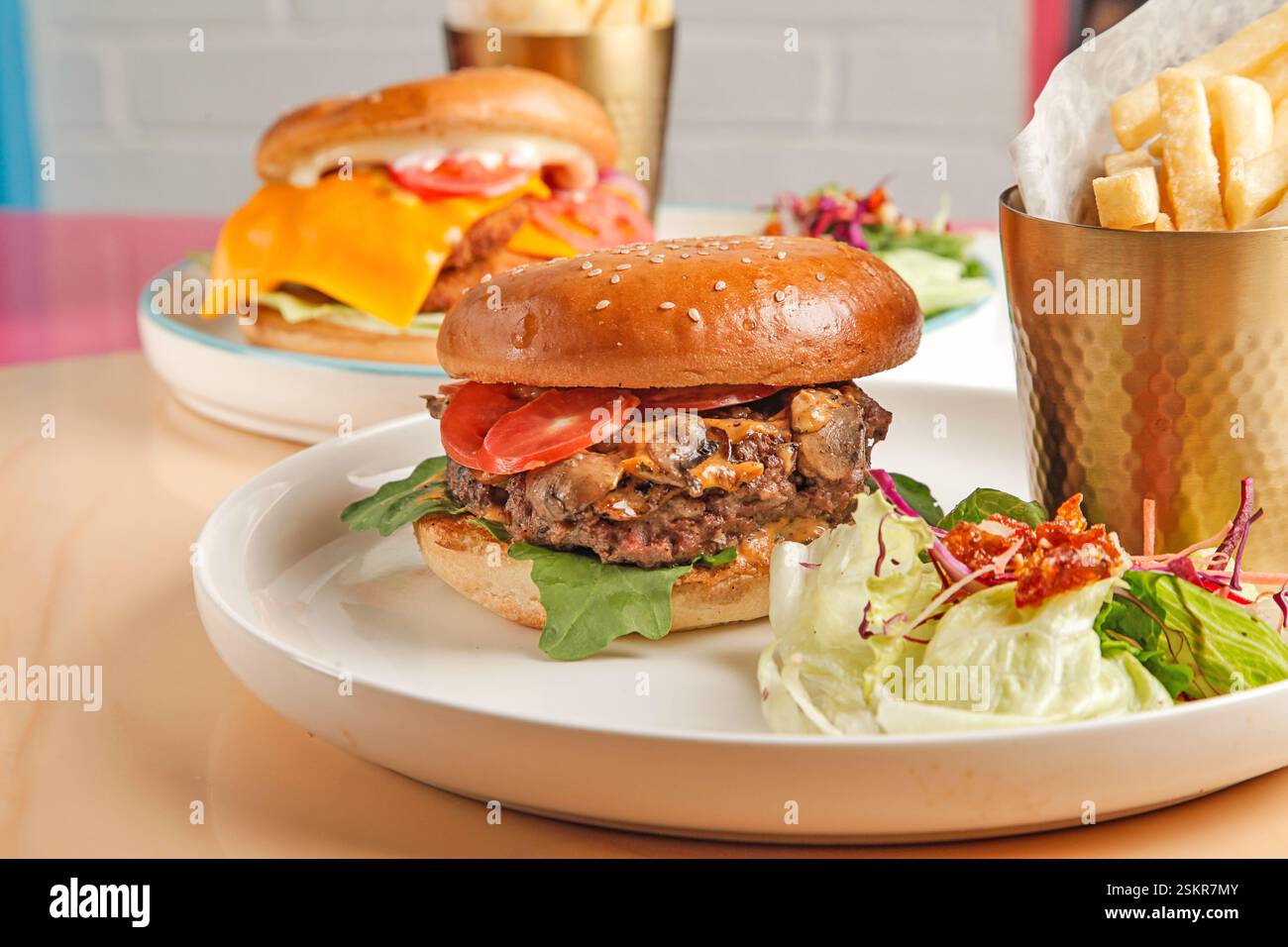 Hamburger gourmet di manzo e pollo fritto serviti con patatine fritte tagliate a mano su un bicchiere di metallo dorato e un pizzico di verdure. Foto Stock